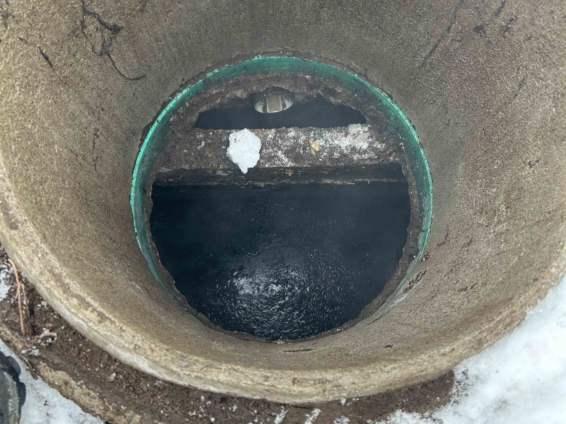 Tuyau en béton ouvert avec un rebord vert, contenant de l'eau sombre ou de la boue.