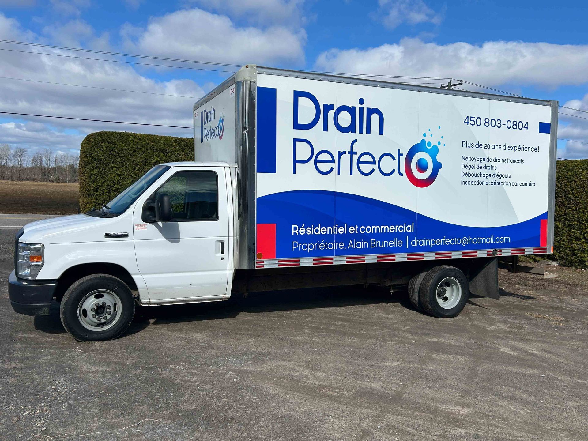 Camionnette de service White Drain Perfect avec logo bleu, garée à l'extérieur sur un terrain gravillonné.