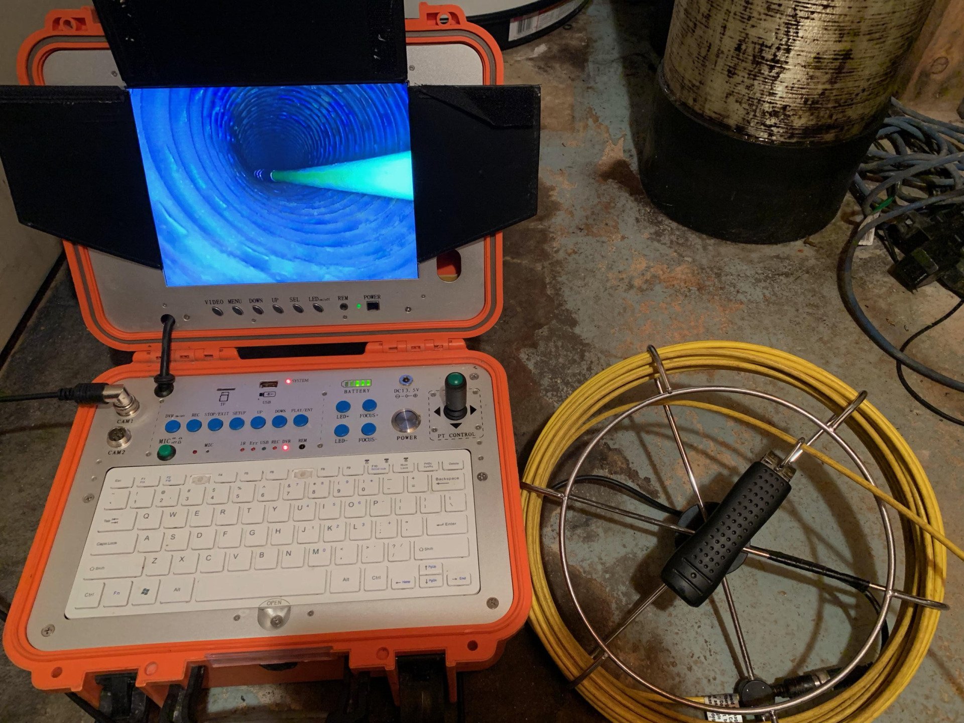 Un écran portable orange et un clavier blanc dans une mallette robuste, à côté d'un câble enroulé jaune, posés au sol.