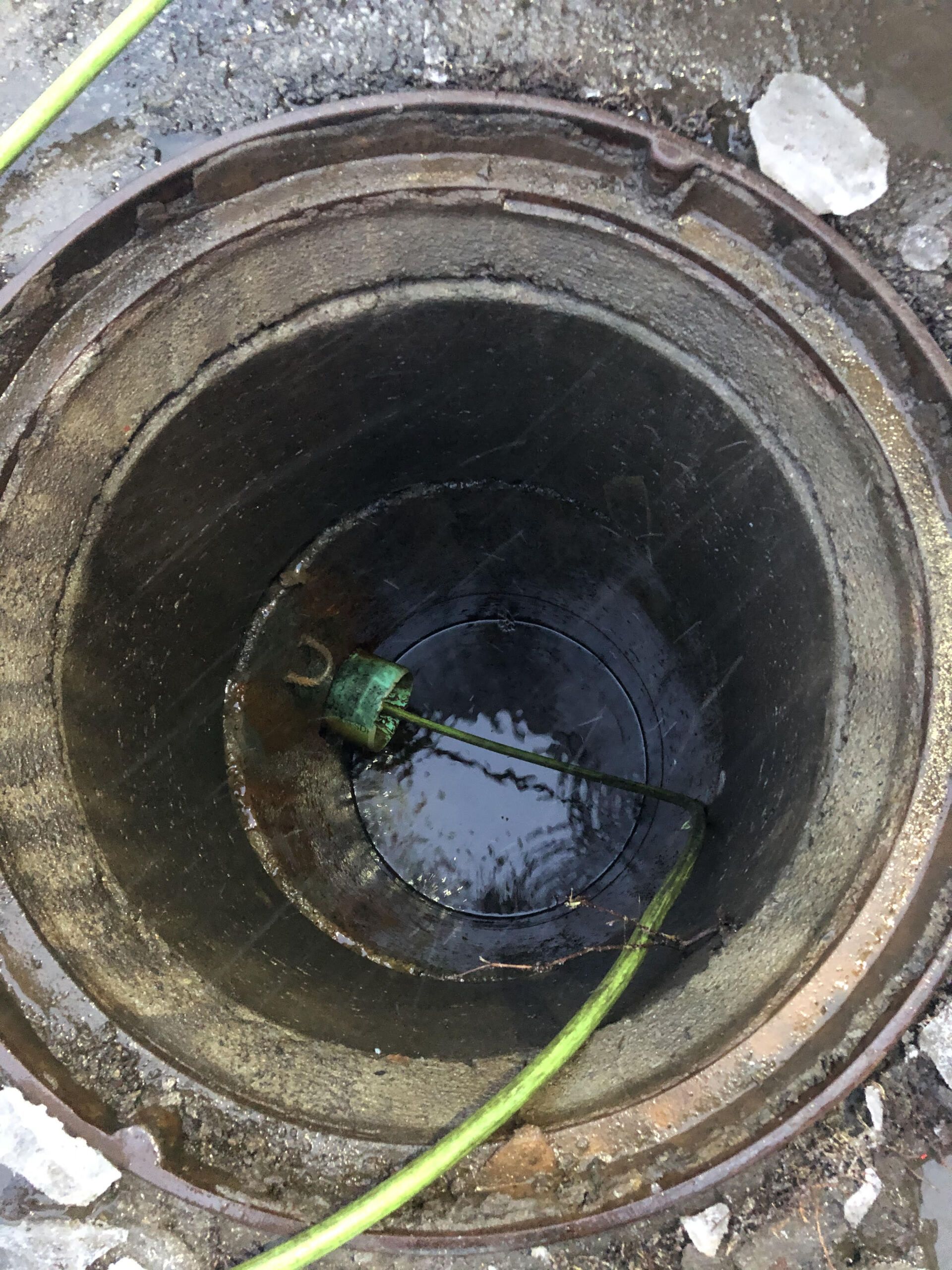 Ouvrir une bouche d'égout contenant de l'eau sombre et un tuyau ou un câble vert à l'intérieur