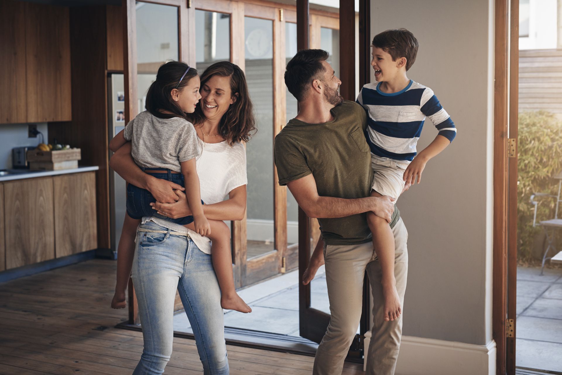 Family standing together in a bright modern room, adults holding two children near large windows.