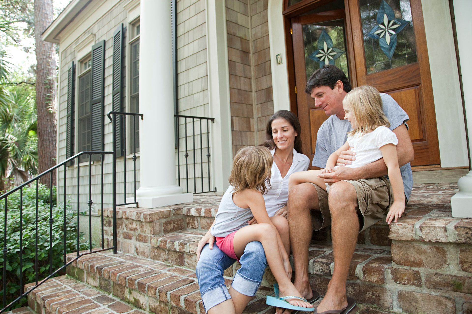 Family sitting on front steps of a house, smiling and talking together