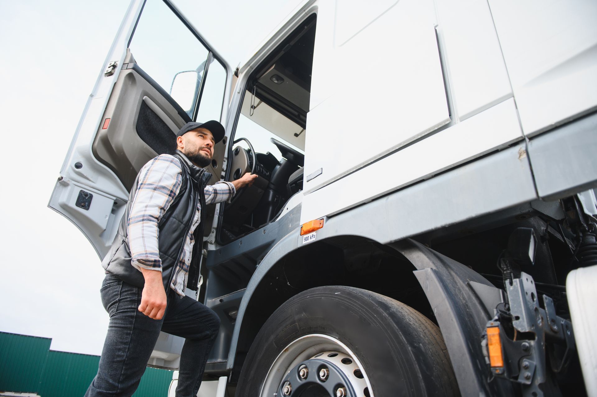 Truck driver climbing into a white semi-truck cab from the side steps.