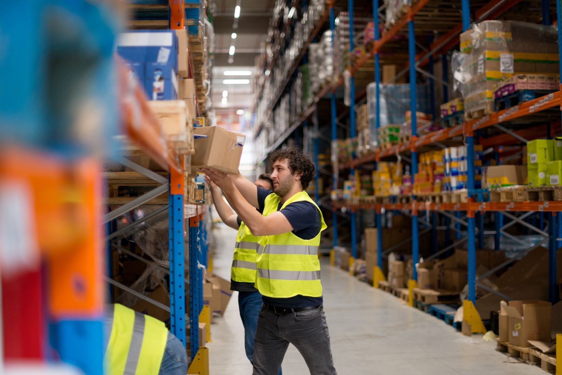 Worker in a high-visibility vest stocking shelves in a warehouse aisle