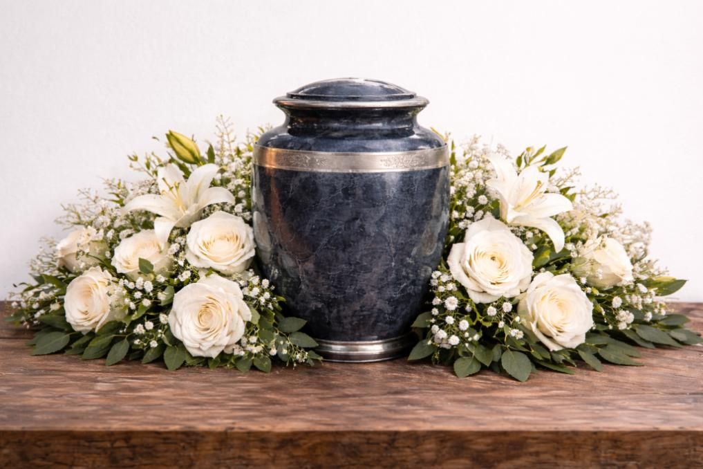 Decorative urn surrounded by white roses and lilies on a wooden table, reflecting caring services from a Renton, WA funeral home and cremations provider.