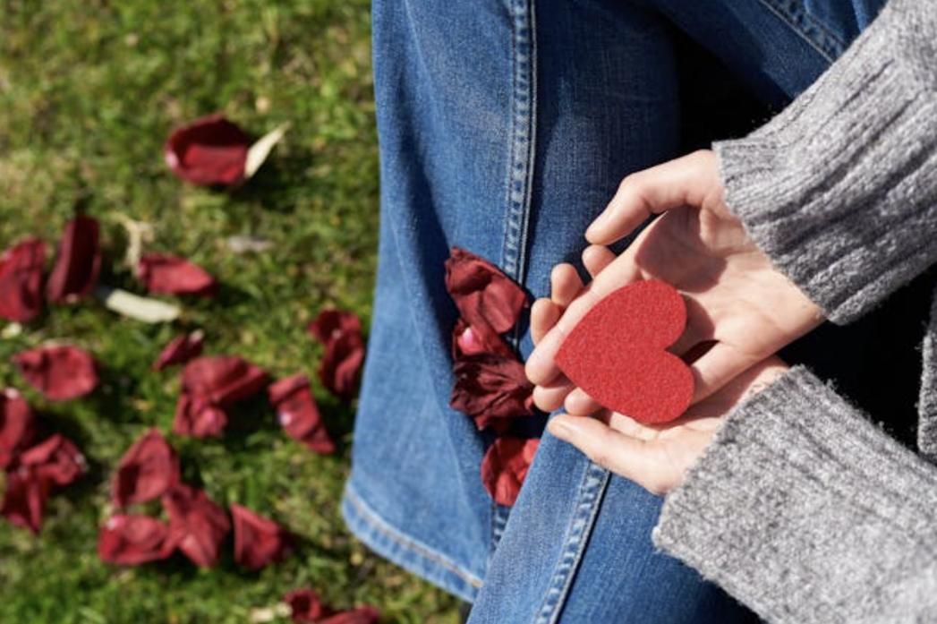 Hands holding a small red heart with rose petals on the grass, symbolizing compassionate care from a Renton, WA funeral home and cremations provider.
