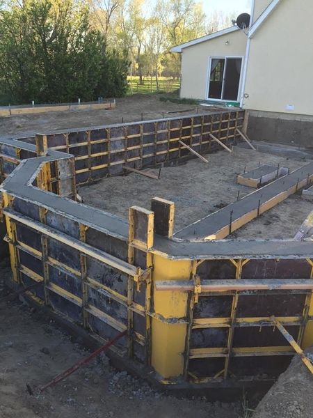 Concrete foundation forms for a curved patio or pool deck beside a house, with yellow and black bracing.