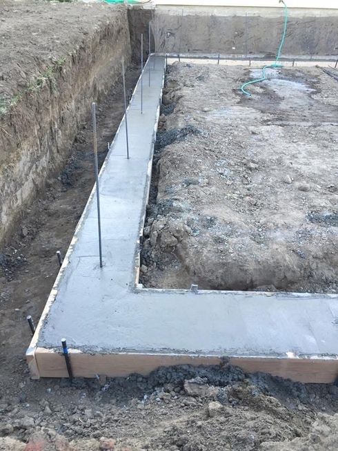Fresh concrete foundation footing forming an L-shape in a dirt excavation site