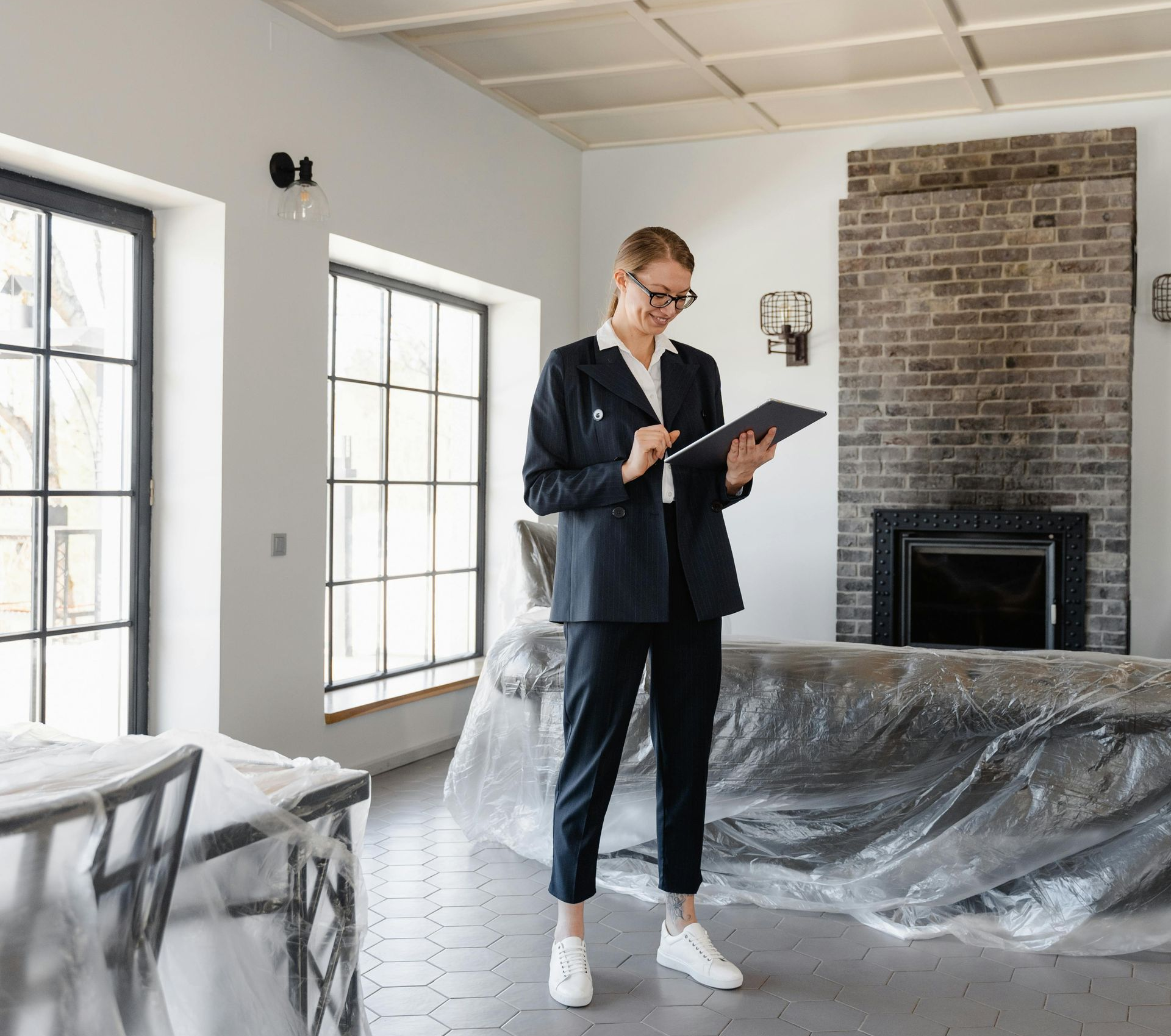 Woman in suit inspecting a room with a tablet, furniture covered in plastic.
