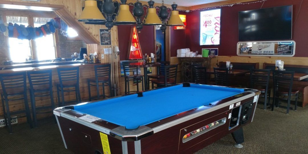 A pool table in a bar with a blue cloth.