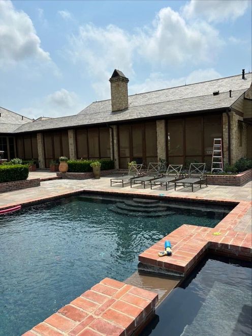 Backyard swimming pool with lounge chairs beside a brick patio and house under a partly cloudy sky