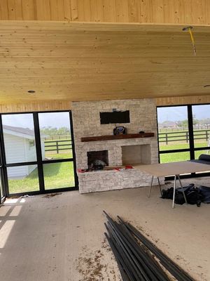 Unfinished living room with wood ceiling, stone fireplace, large windows, and construction materials on the floor