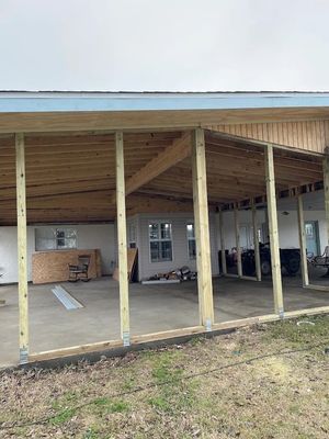 Open-sided wooden shed with exposed beams and concrete floor, partially built and unfinished.