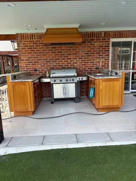 Outdoor brick patio with built-in grill, side counters, and cabinets under a covered roof