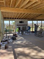 Workers installing an outdoor stone fireplace under a covered pavilion, with tools and materials scattered nearby.