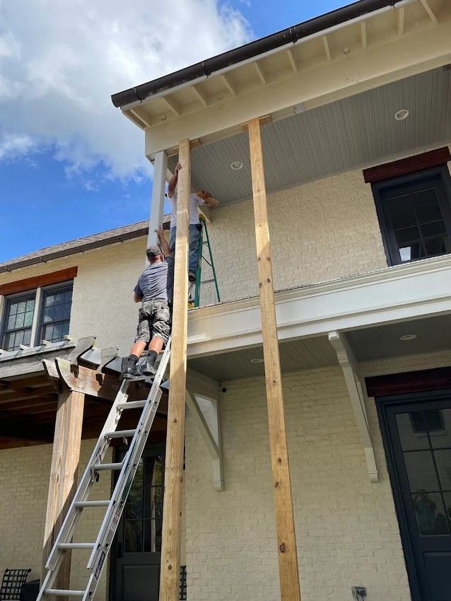 Worker on ladder installing wooden porch supports on a house exterior