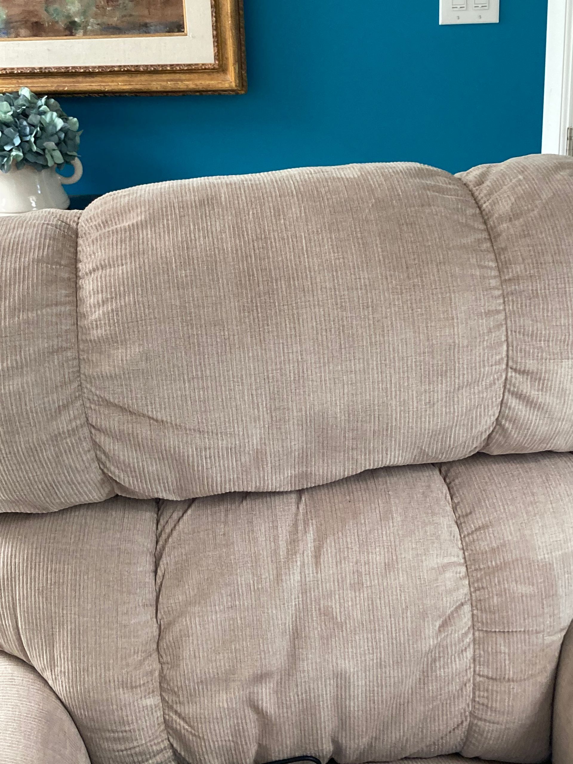 Beige upholstered couch against a teal wall, with a framed picture and blue flowers in the background