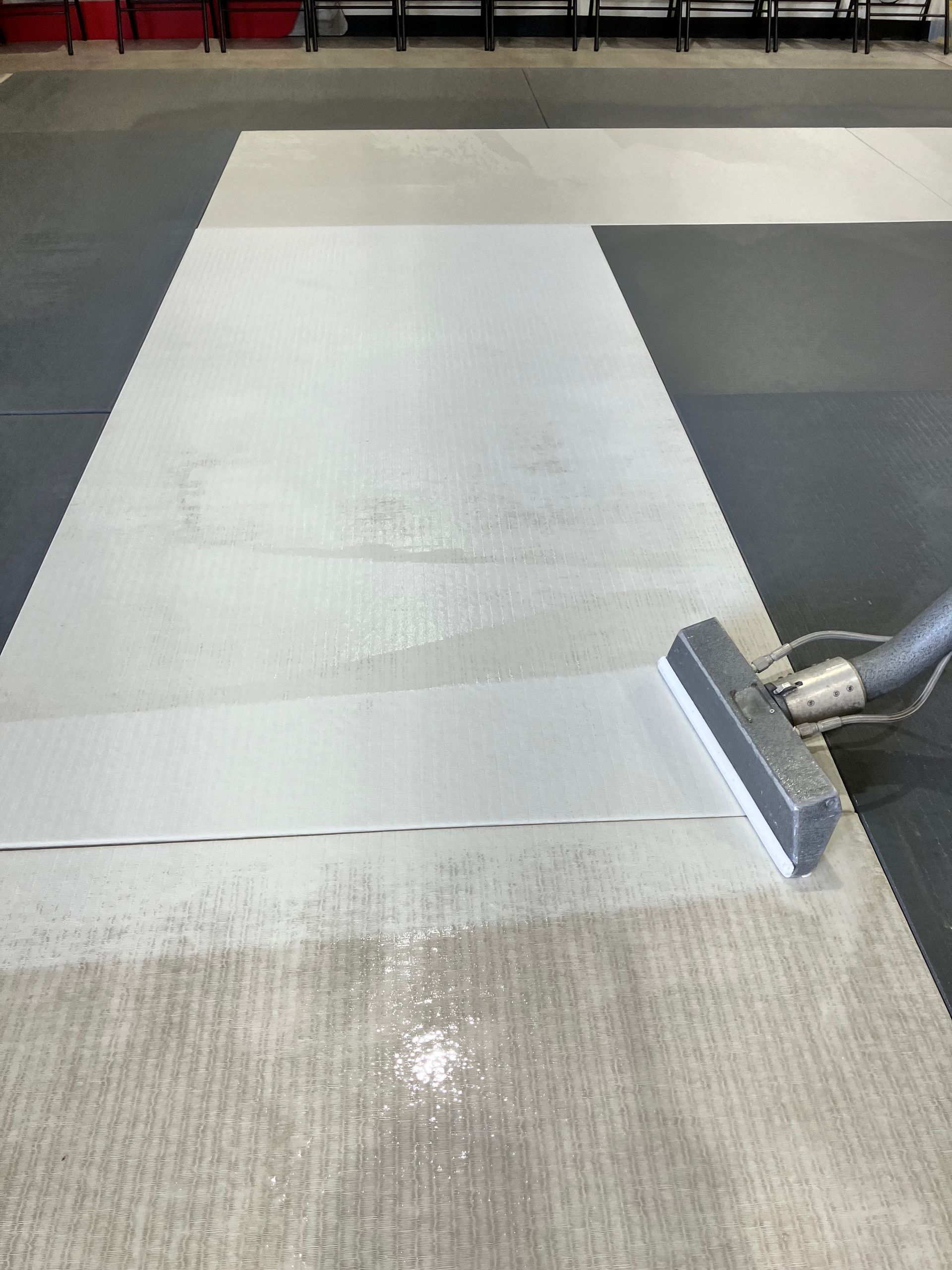 Worker applying white coating to a floor with a squeegee in a tiled indoor area