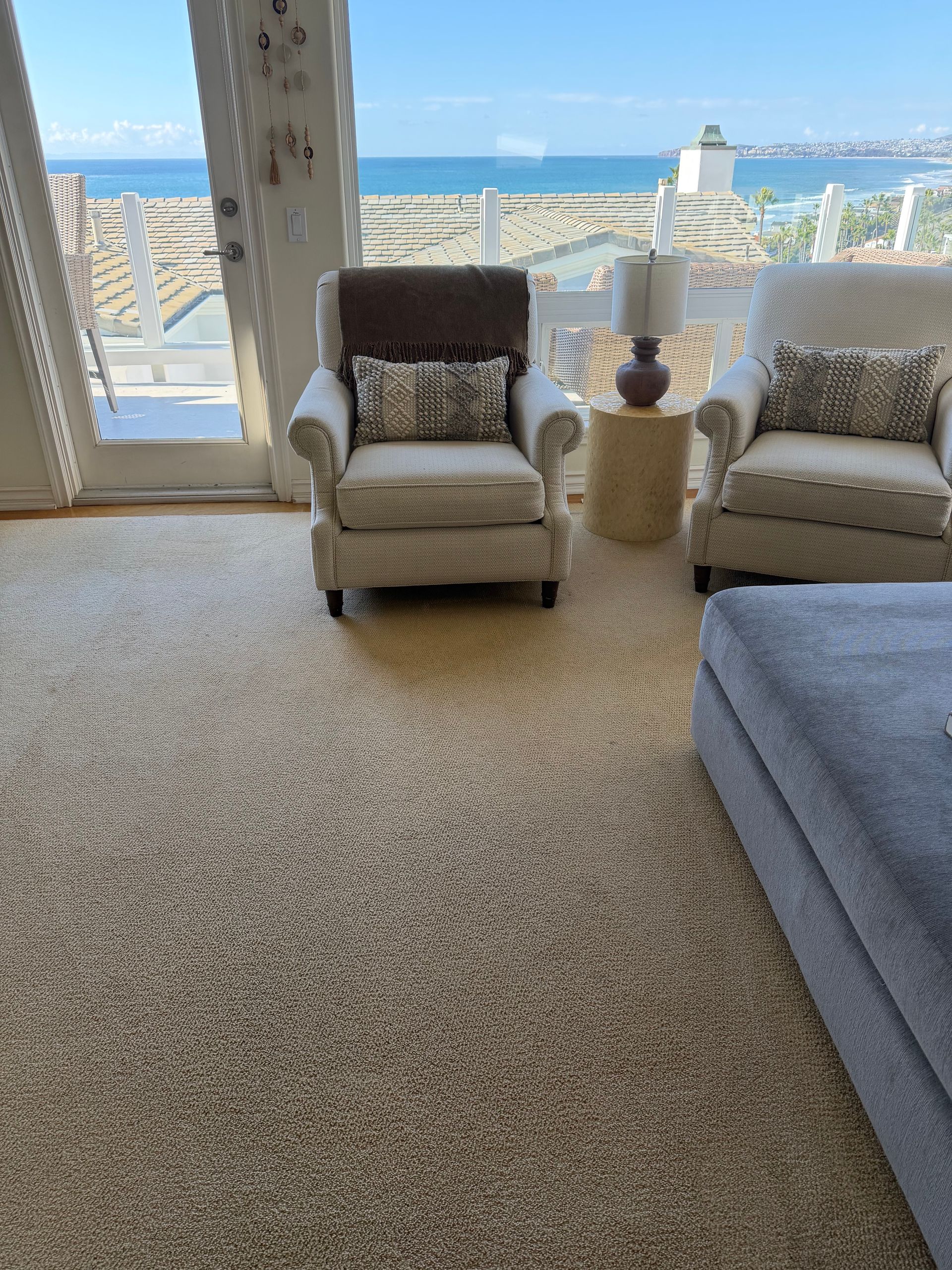 Bright living room with ocean view, two armchairs, side table, and a bed in the foreground