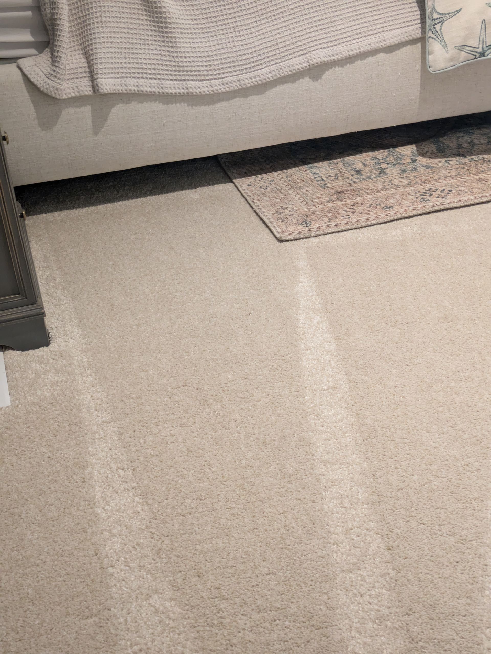 Carpeted room with a bed edge and a small rug on the floor