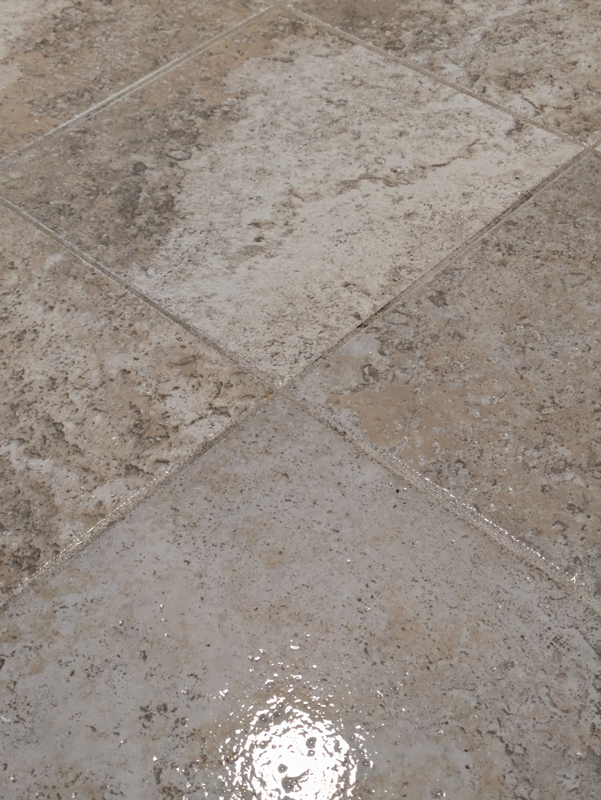 Close-up of wet beige and gray stone tiles with a small puddle reflecting light