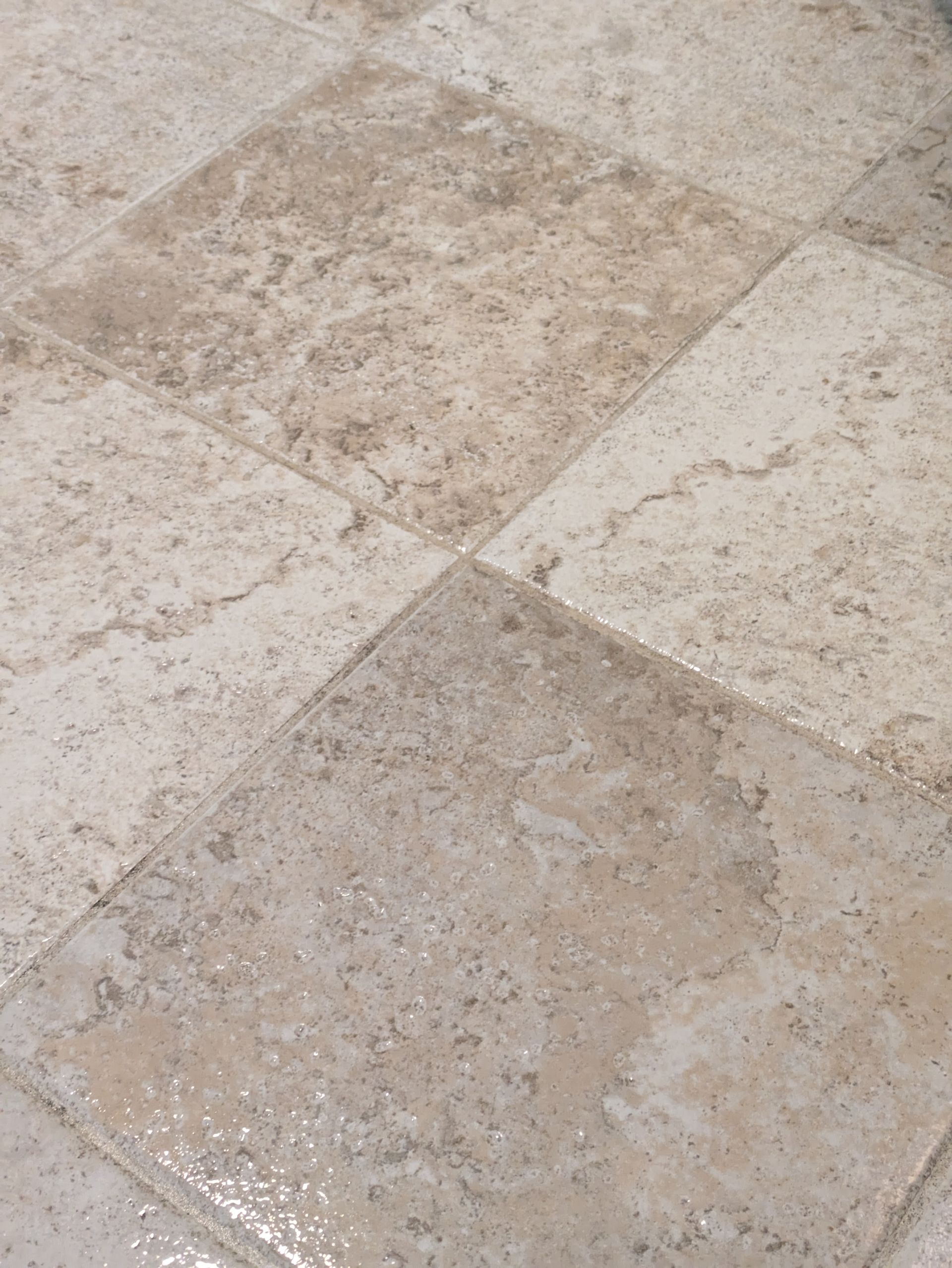 Close-up of beige and gray stone floor tiles with a worn, speckled texture.