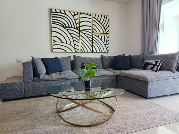 Modern living room with gray sectional sofa, glass coffee table, and abstract wall art.