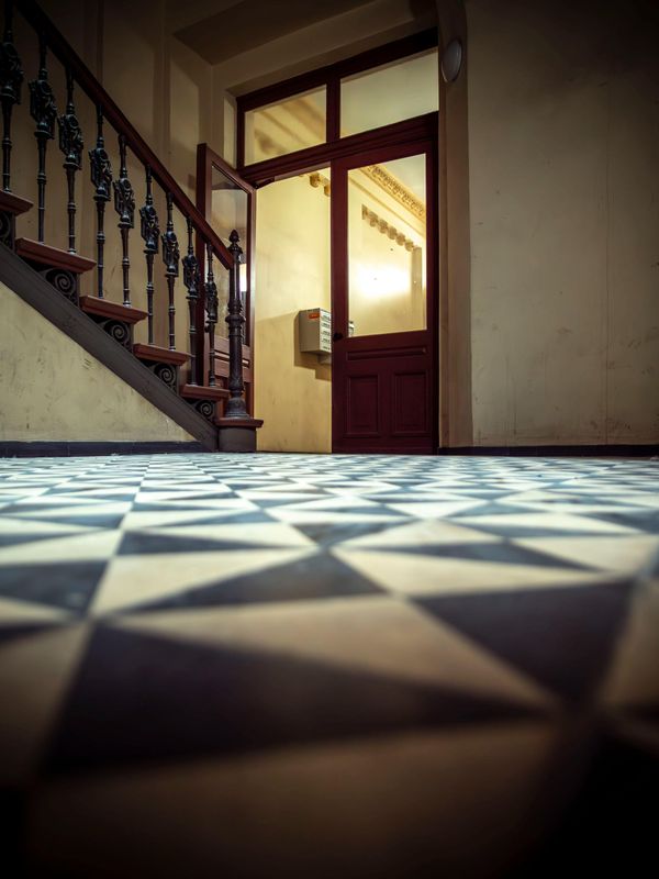 Staircase in a dim hallway, with a bright open doorway and black-and-white patterned floor tiles.