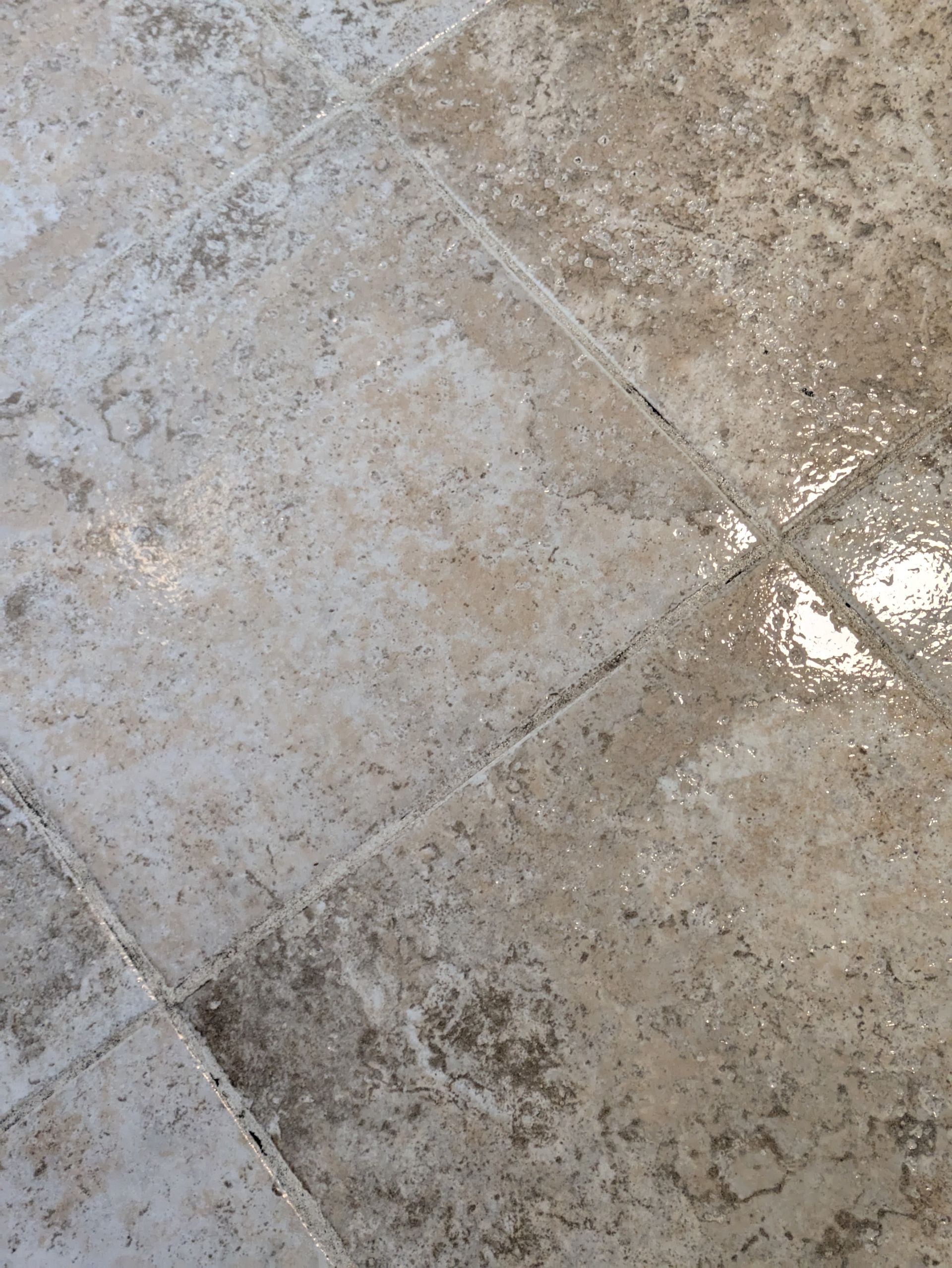 Close-up of a wet beige tiled floor with light reflections and grout lines