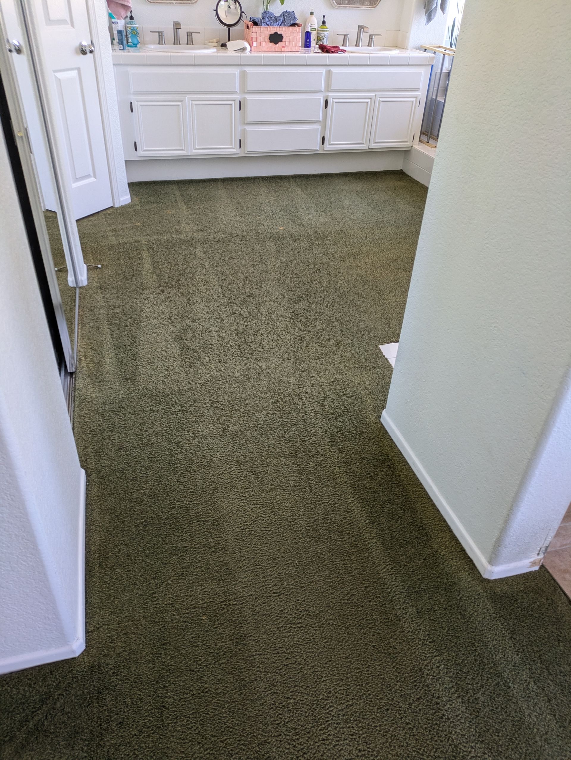 Carpeted hallway leading to a white bathroom vanity with sink and mirror.