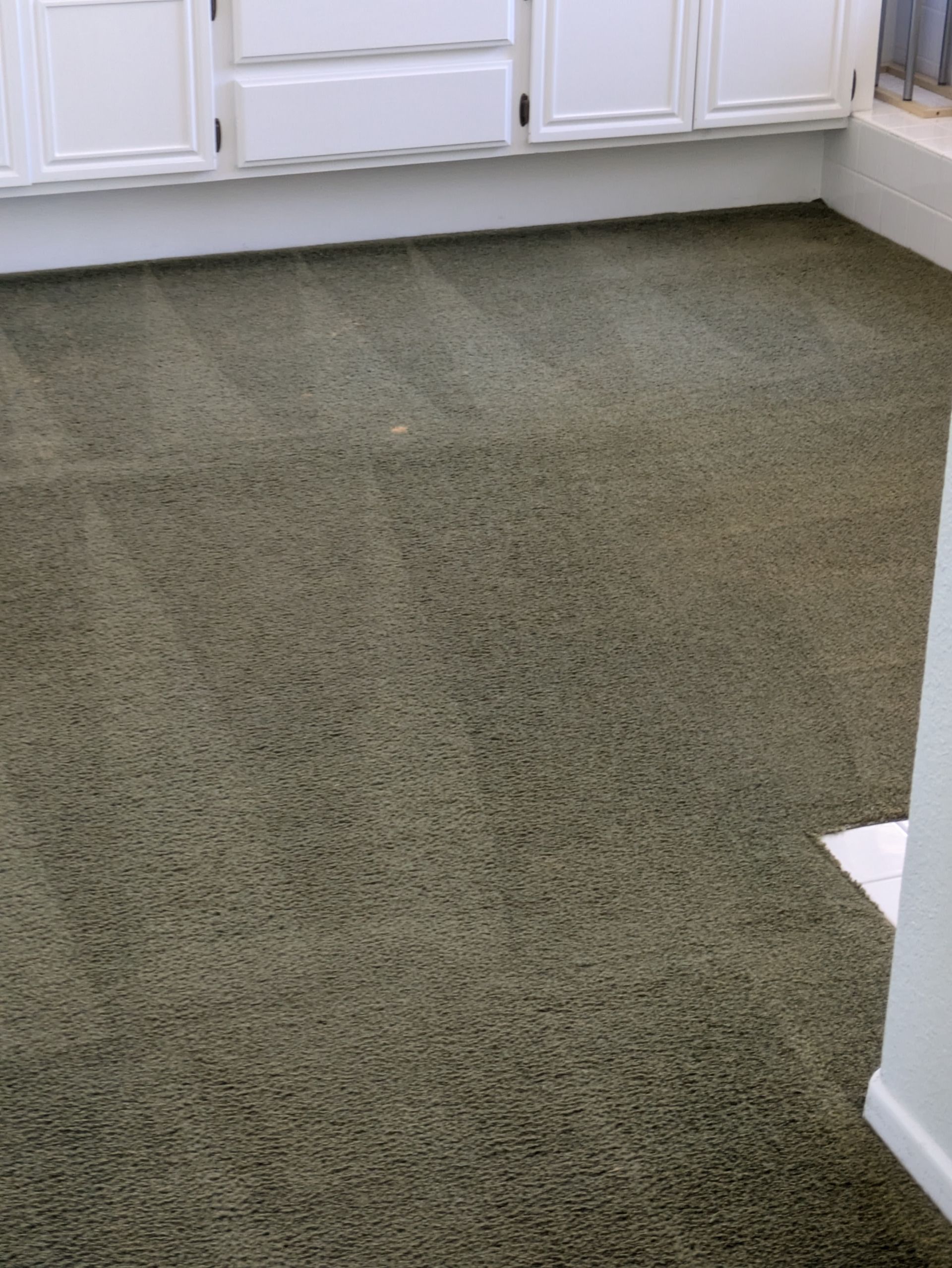 Empty carpeted room with white cabinets and a corner wall.