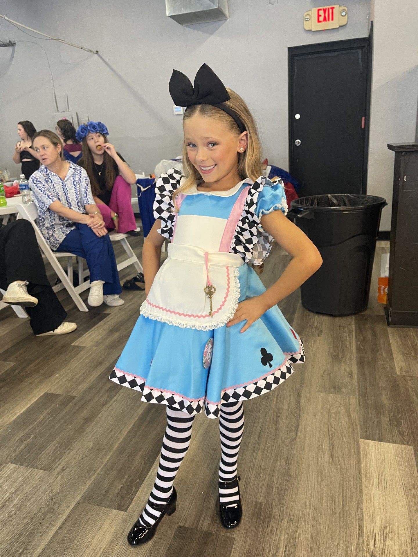 Girl in blue costume posing in a dance studio, with striped stockings and a large black bow.