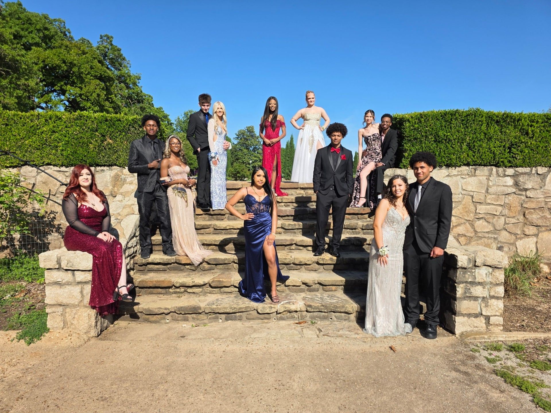 Group of people posing on stone steps outdoors in formal attire under a bright blue sky