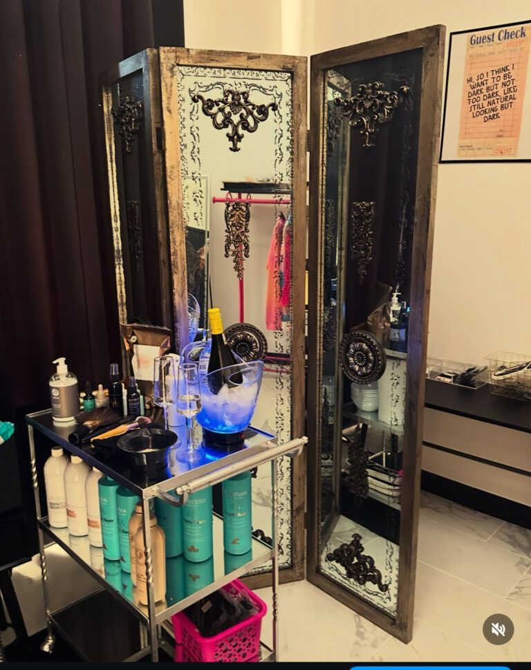 Salon styling station with mirror, shelves, brushes, hair products, and a pink basket on the floor