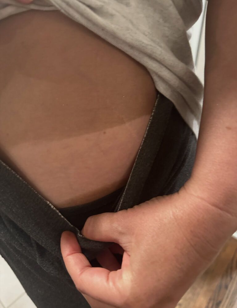 Hand adjusting a black waistband on a beige shirt, showing a close-up of the torso.
