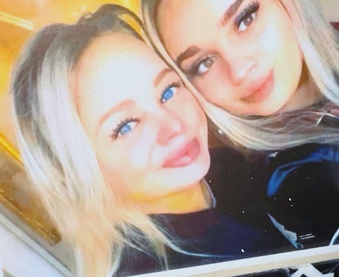 Two smiling women posing closely together in a bright selfie, with one wearing dark clothing and the other blonde.
