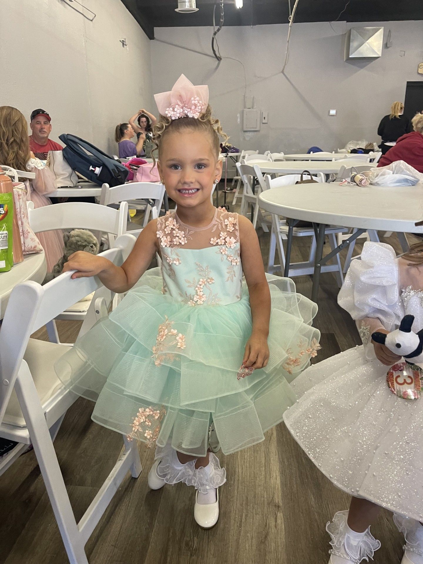 Young child in a mint green dress and bunny ears smiling at a party table