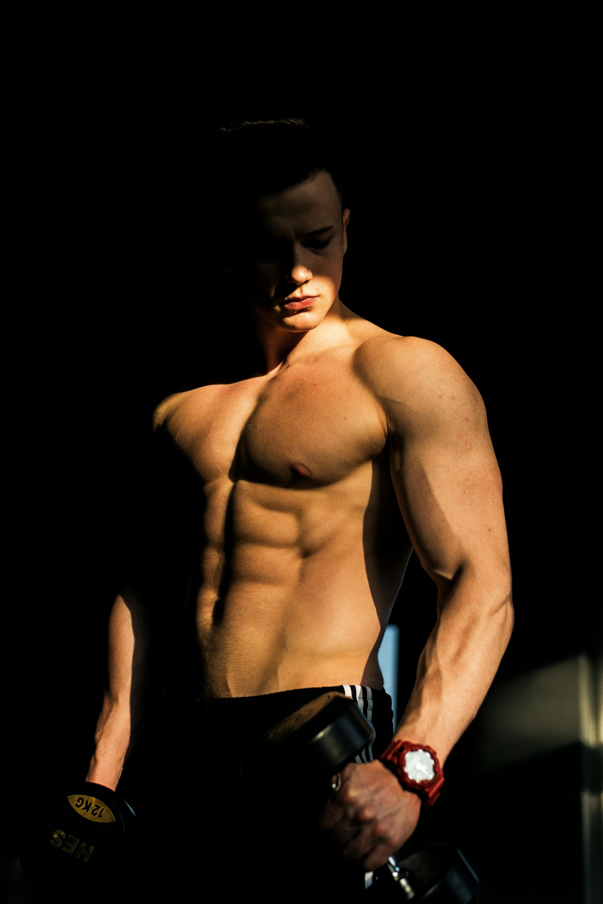 Shirtless muscular man in dark pants, posed against a black background with dramatic lighting