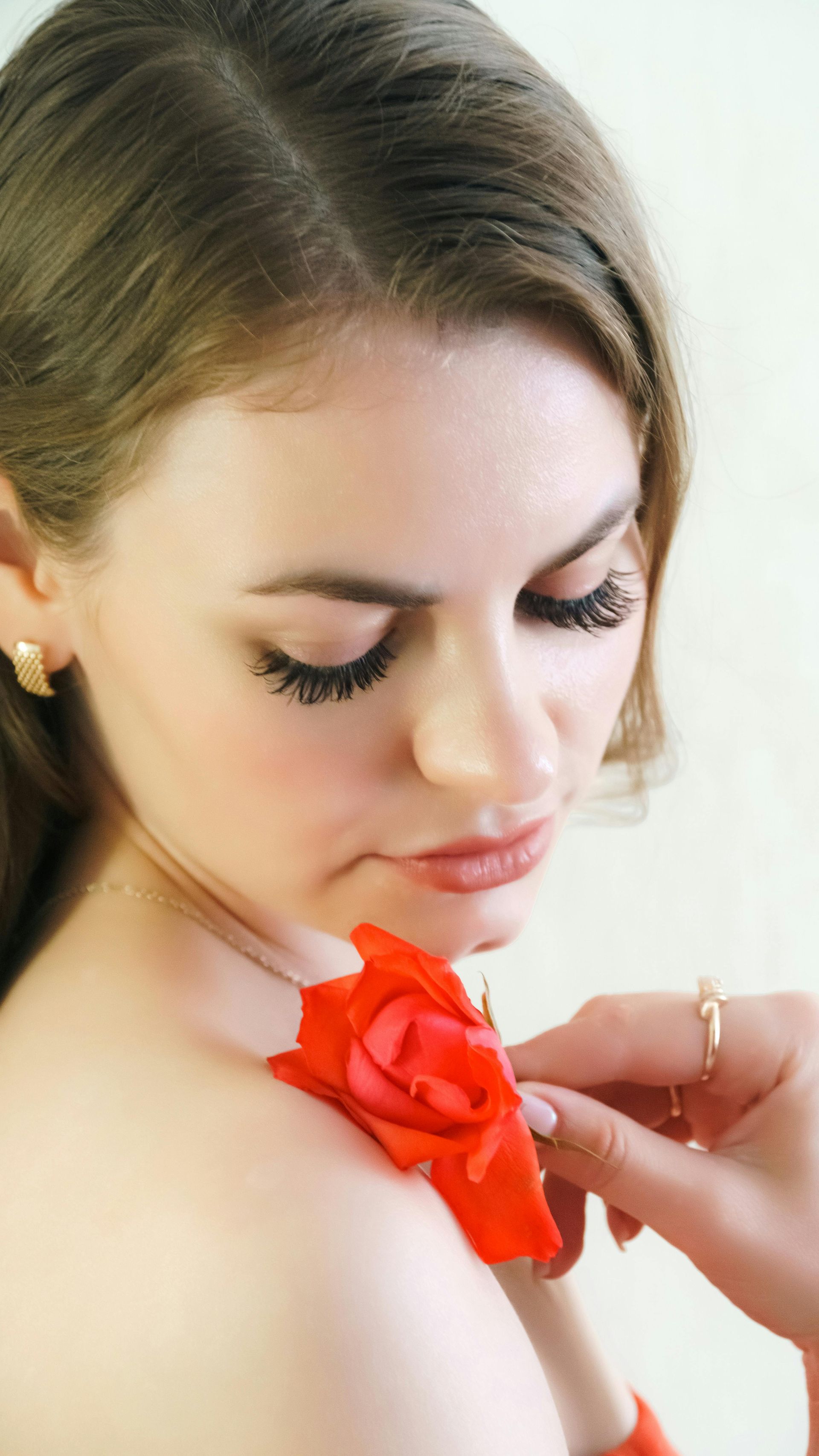 Woman with eyes closed as a hand adjusts a bright red flower on her shoulder
