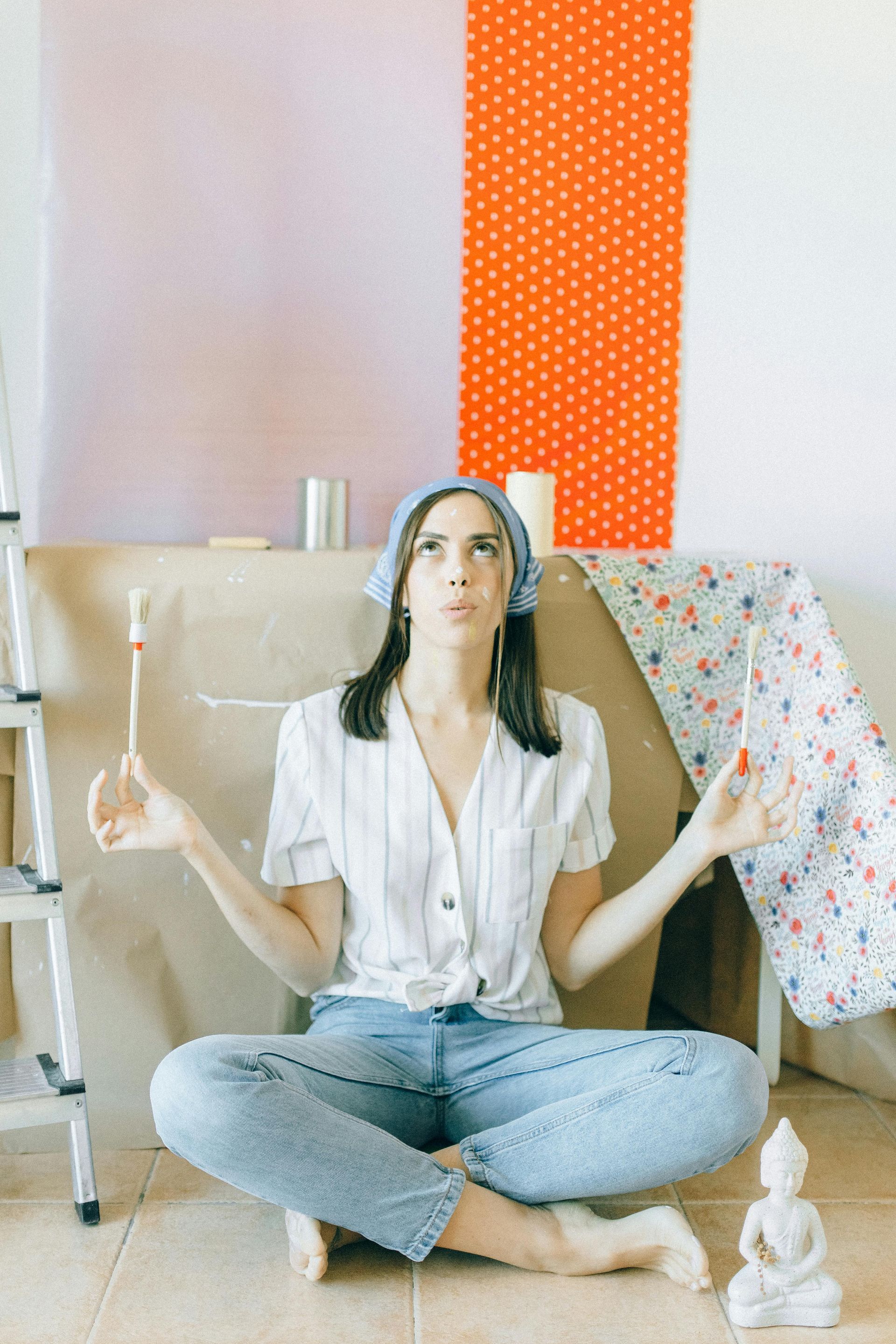 Woman sitting cross-legged on a floor cushion, meditating beside a beige couch and floral drape in a bright room