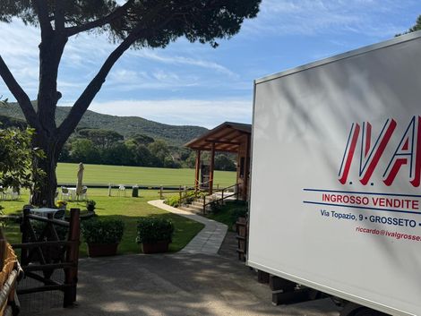 Un carrello elevatore Toyota arancione e un transpallet elettrico arancione più piccolo, entrambi parcheggiati in un corridoio di stoccaggio di un magazzino industriale.