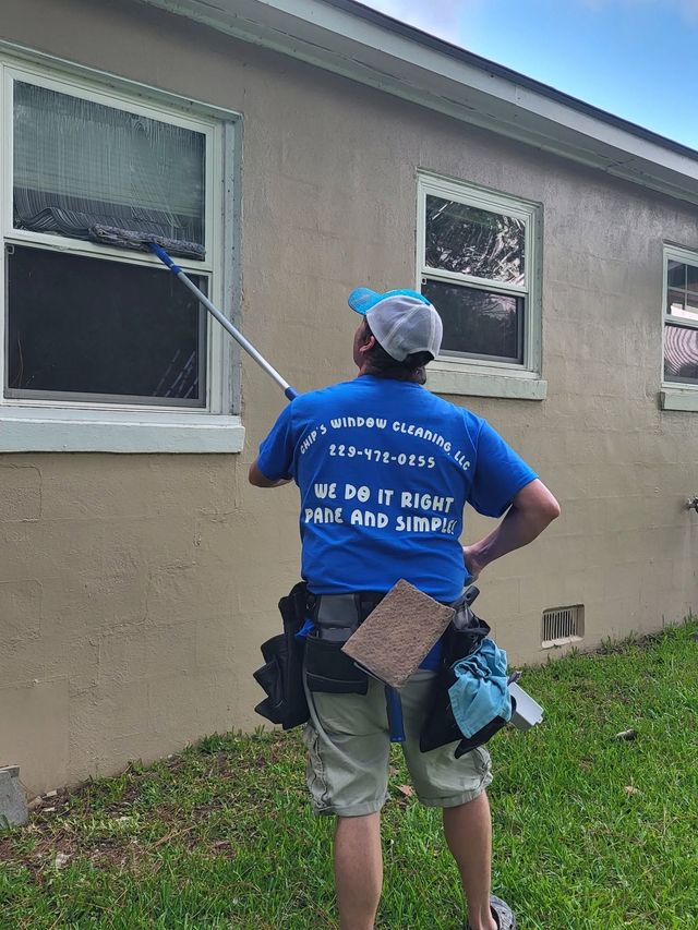 Worker in blue shirt pressure-washing a house exterior with a long wand.