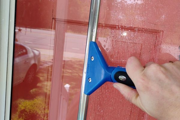 Hand using a blue squeegee on a red glass door window