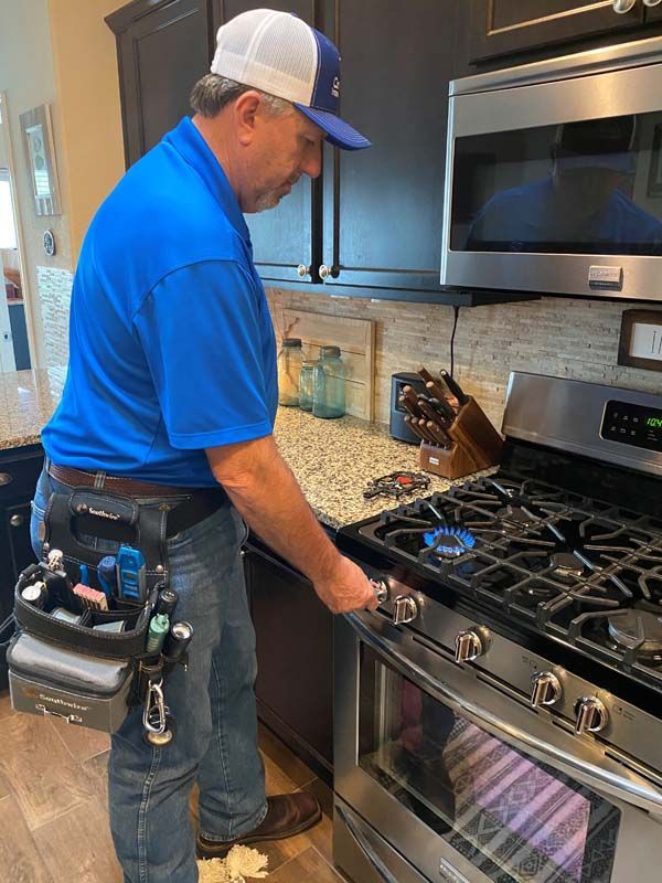 A man in a blue shirt is working on a stove in a kitchen.