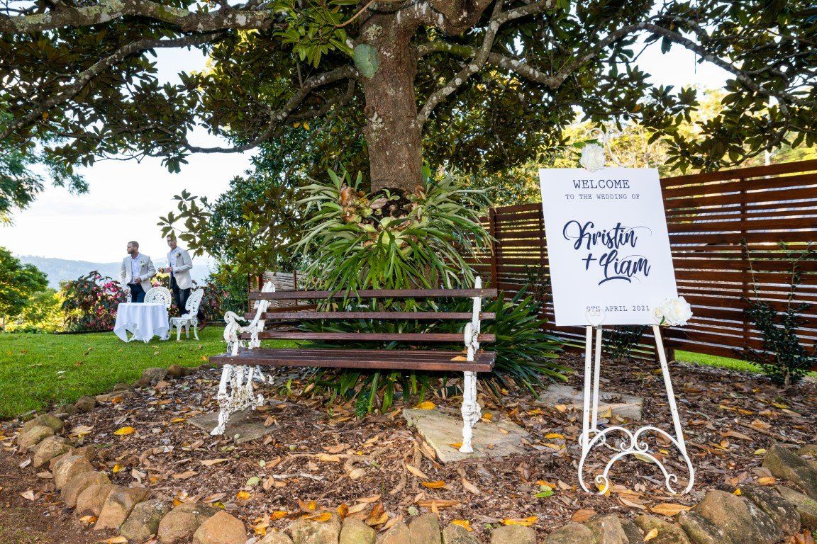 a wooden bench is sitting under a tree next to a welcome sign .