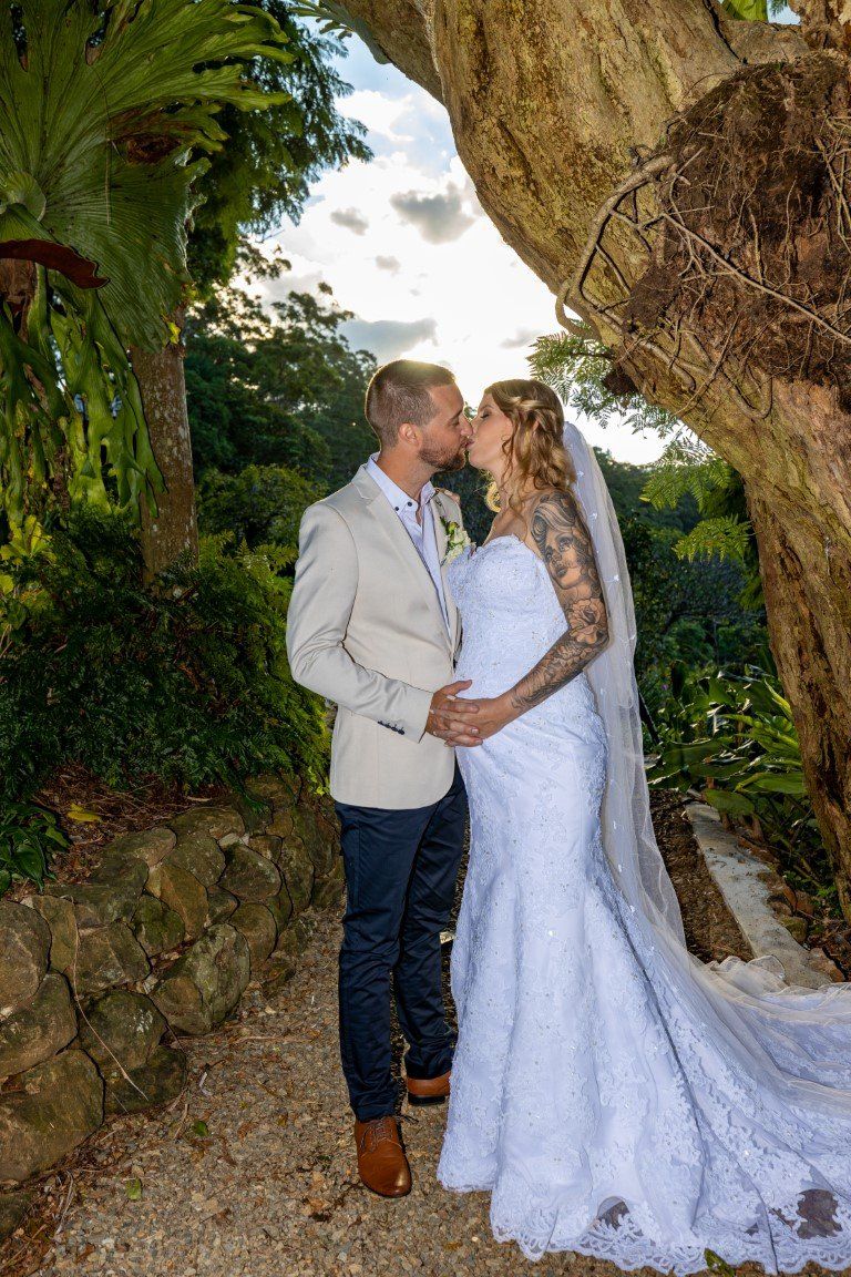 a bride and groom are kissing under a tree .
