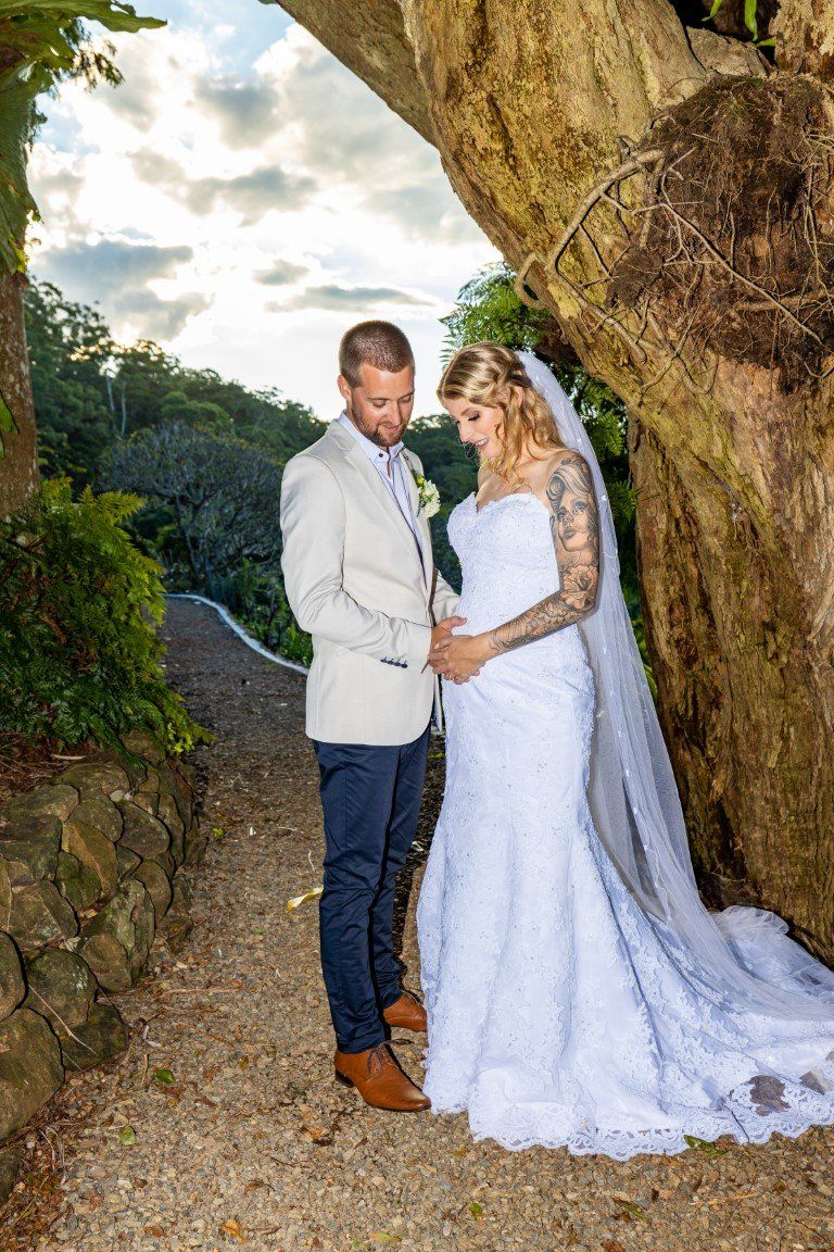 a bride and groom are standing under a tree holding hands .