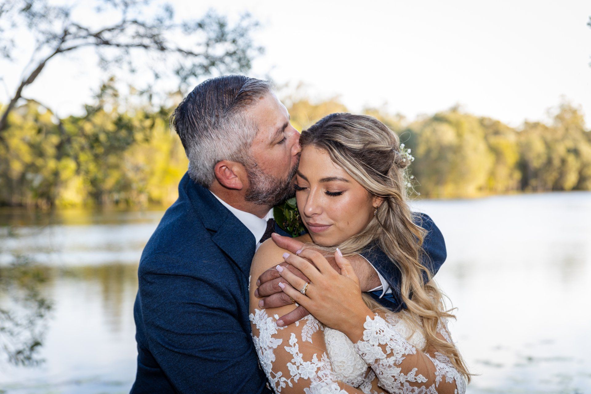 a man is kissing a woman on the forehead in front of a lake .