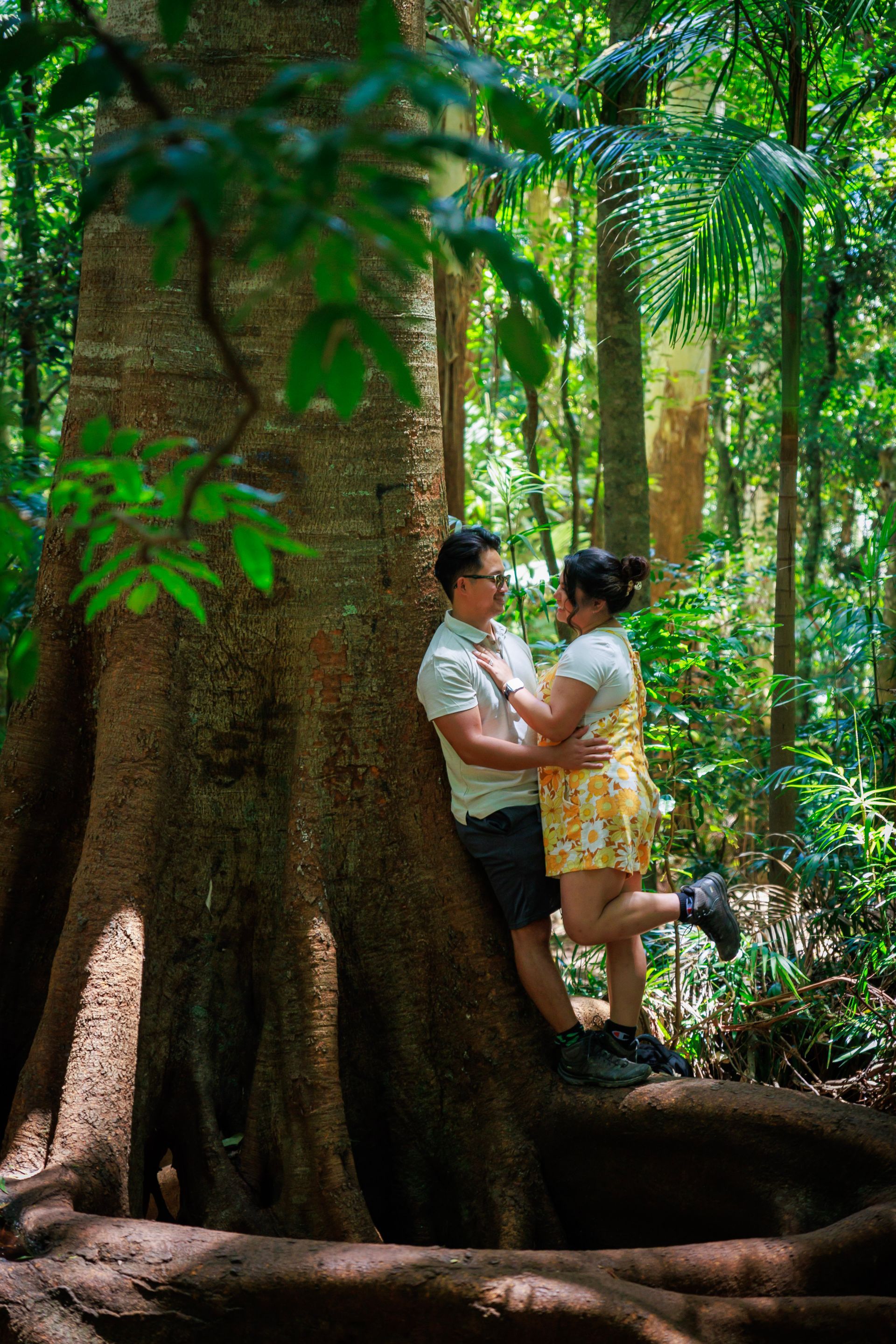 a man and a woman are leaning against a tree in the woods .