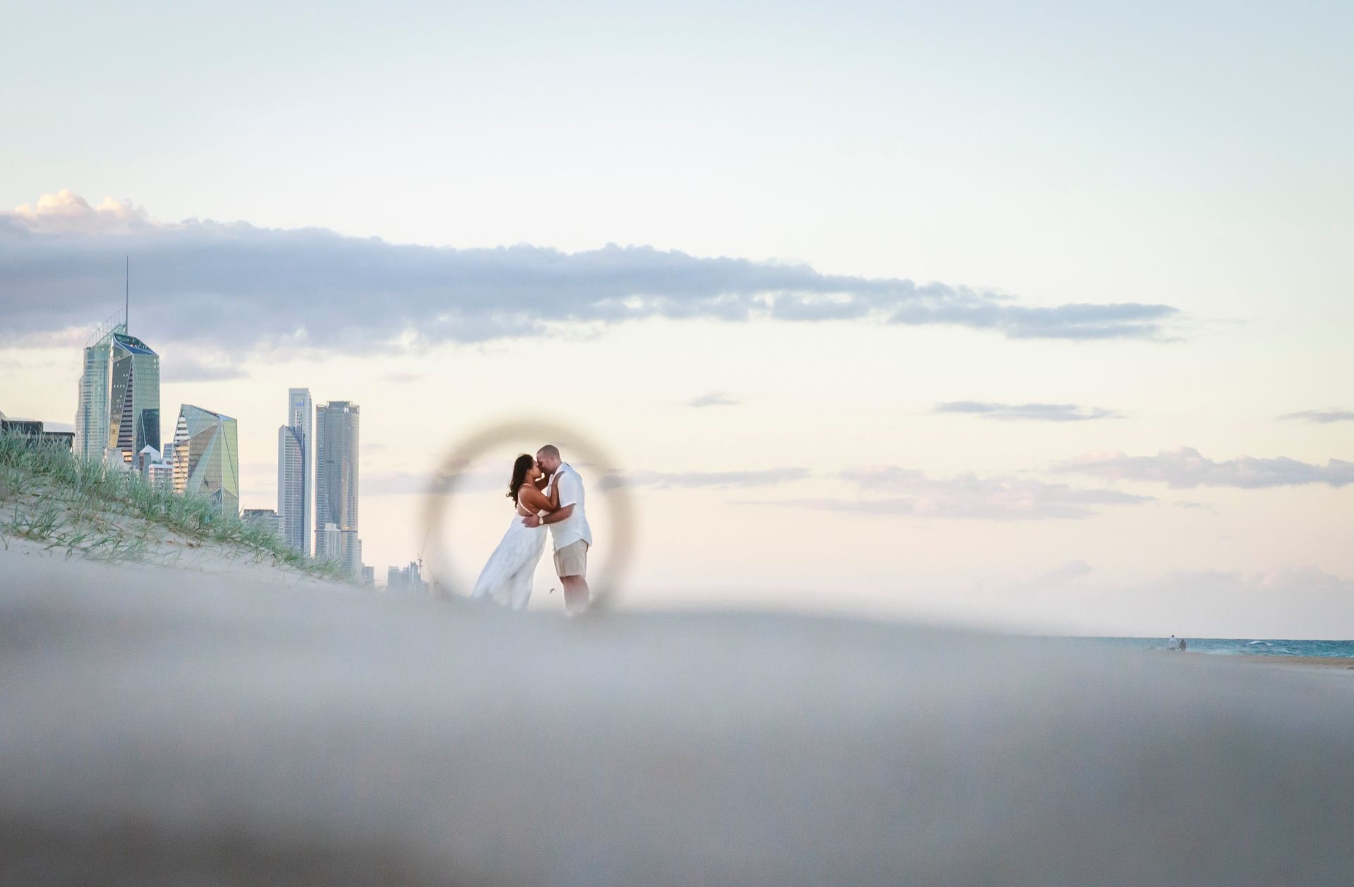 a man and woman are kissing on a beach with a city skyline in the background .